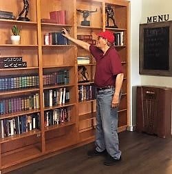 A person wearing a red cap and shirt selecting a book from a tall wooden bookshelf.