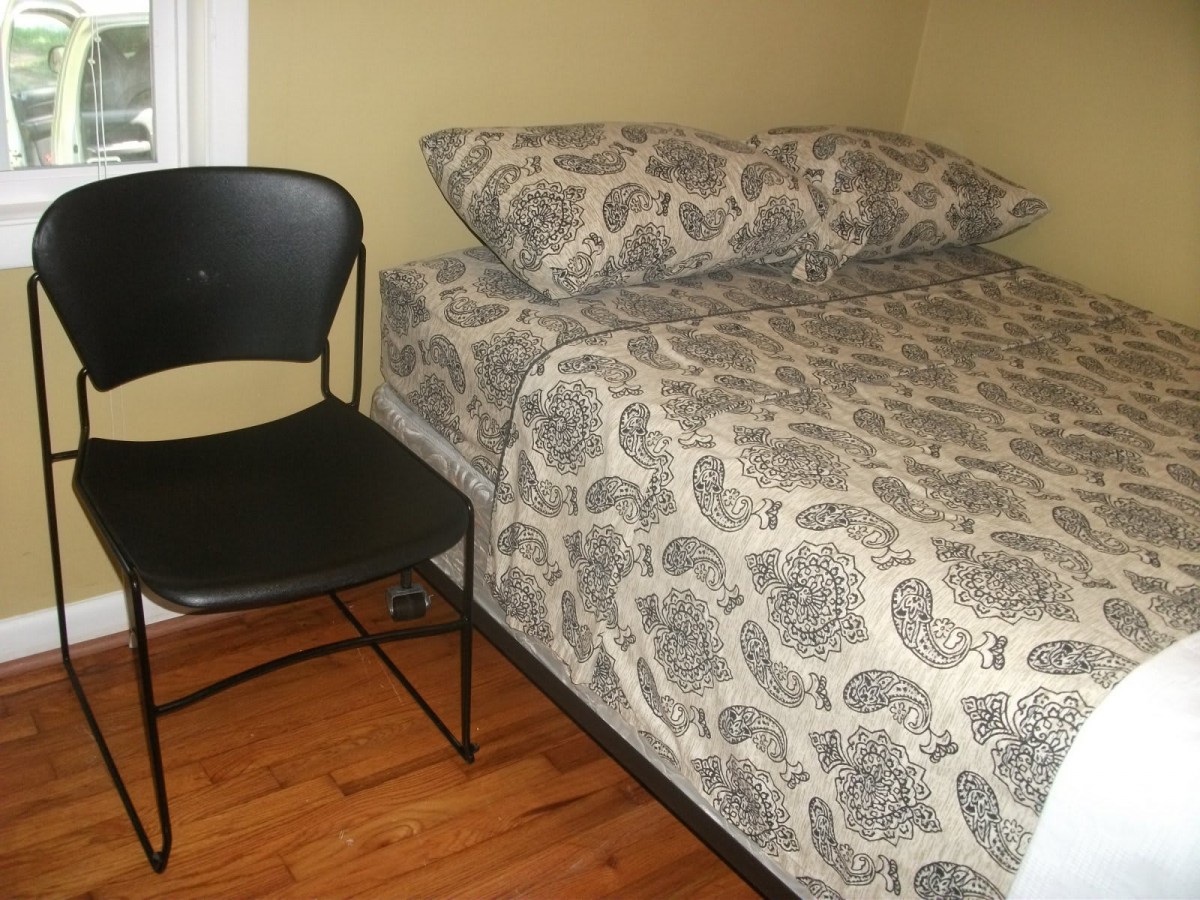 A neatly made bed with patterned bedding next to a black chair in a simple bedroom.