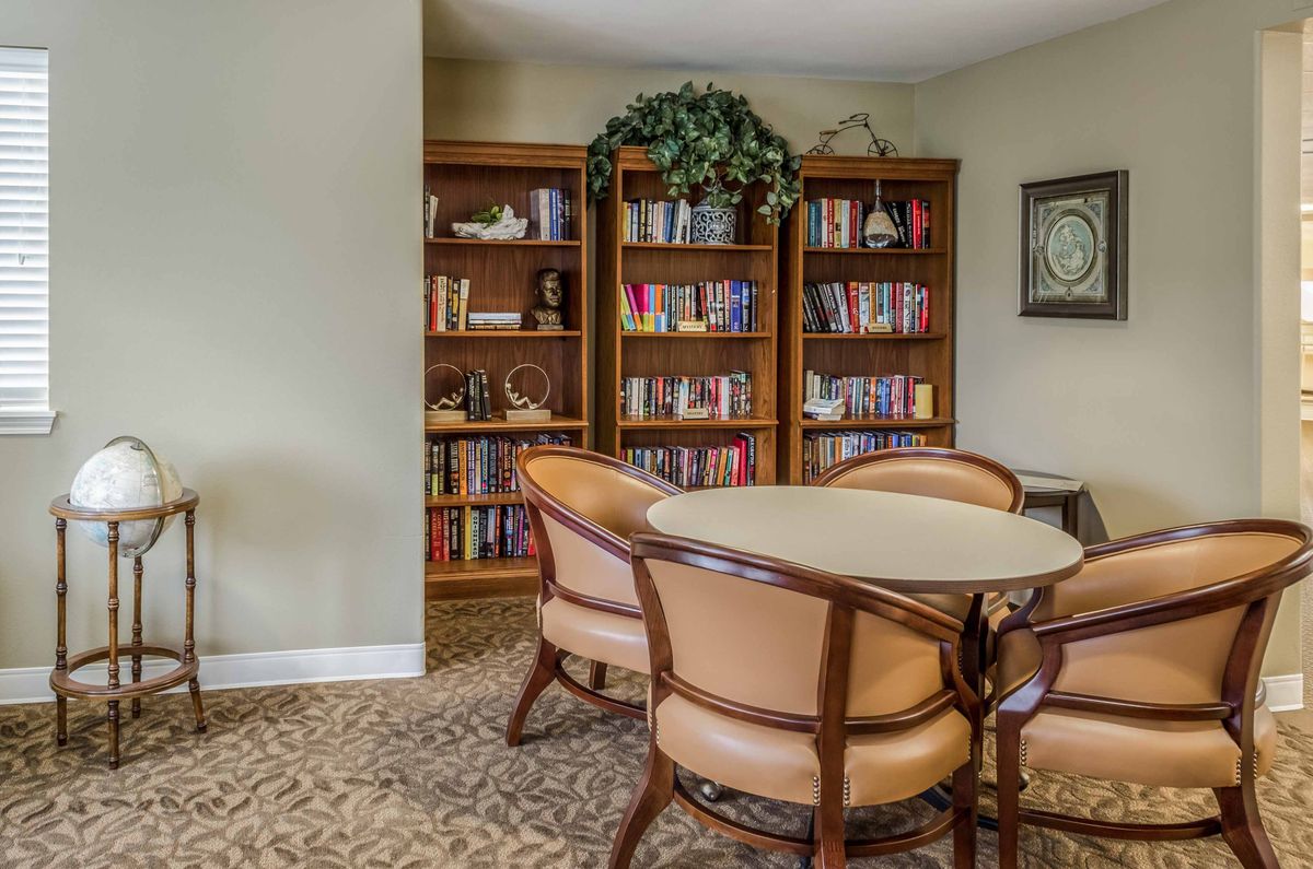 A cozy library room with bookshelves and a round table surrounded by chairs.