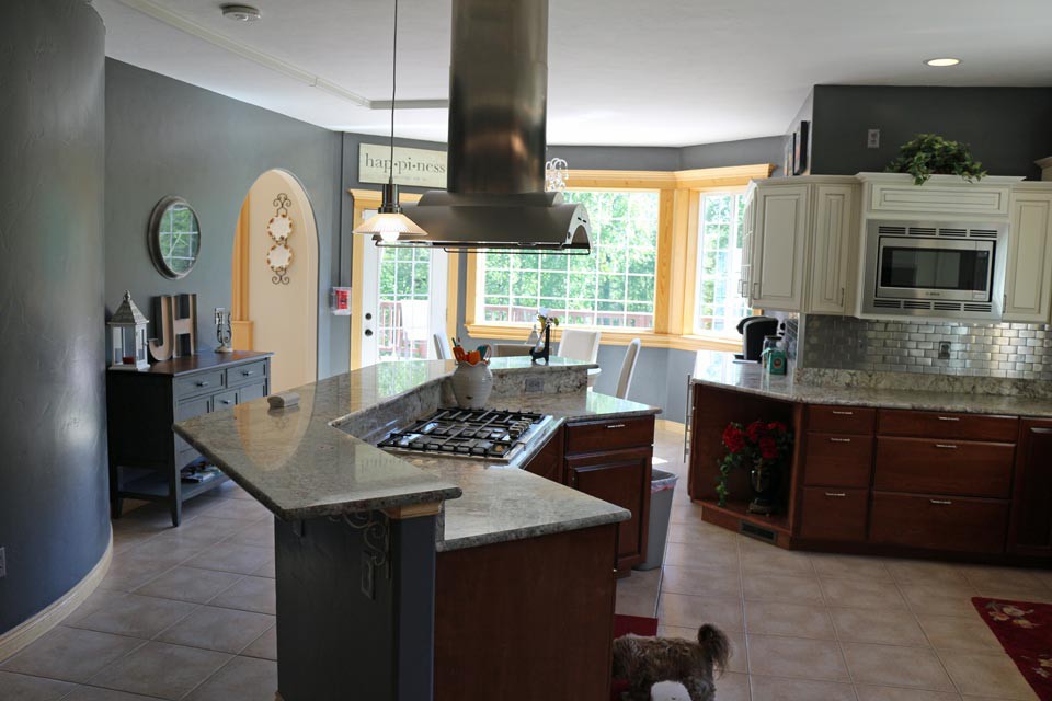A modern kitchen with stainless steel appliances and a central island, featuring large windows and wooden cabinets.
