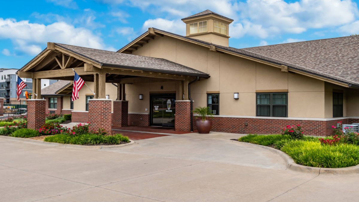 Entrance to a building with an American flag and landscaped surroundings.