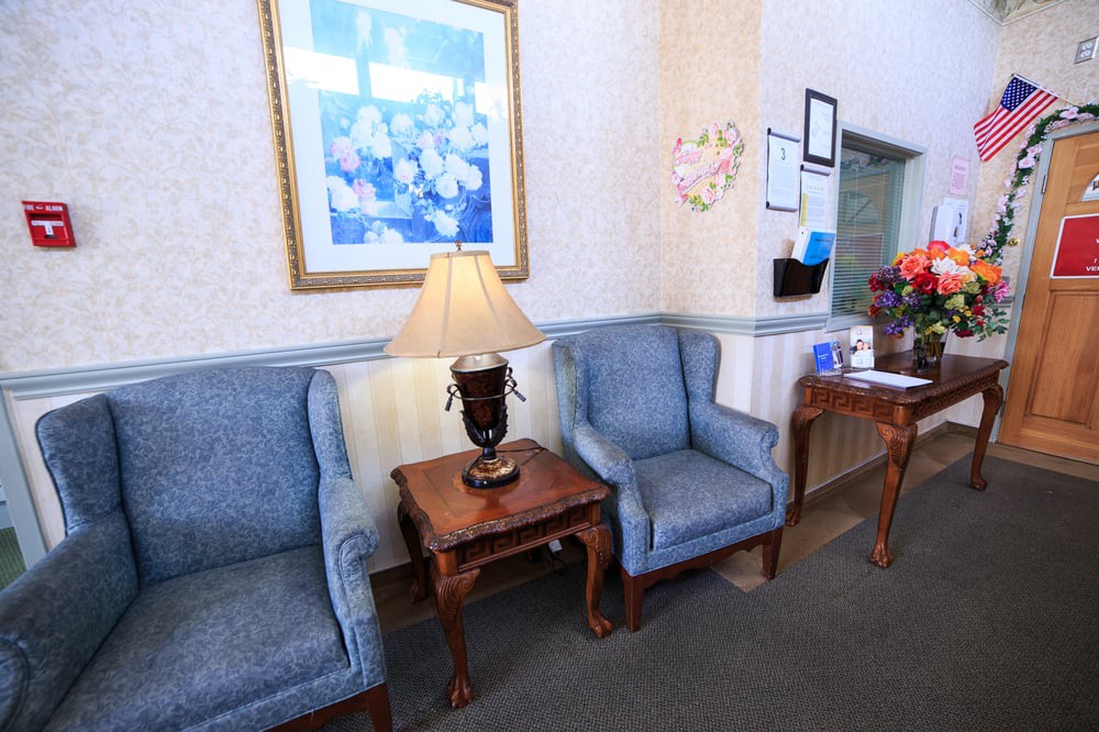 A cozy waiting room with two blue chairs and a wooden table topped by a lamp.