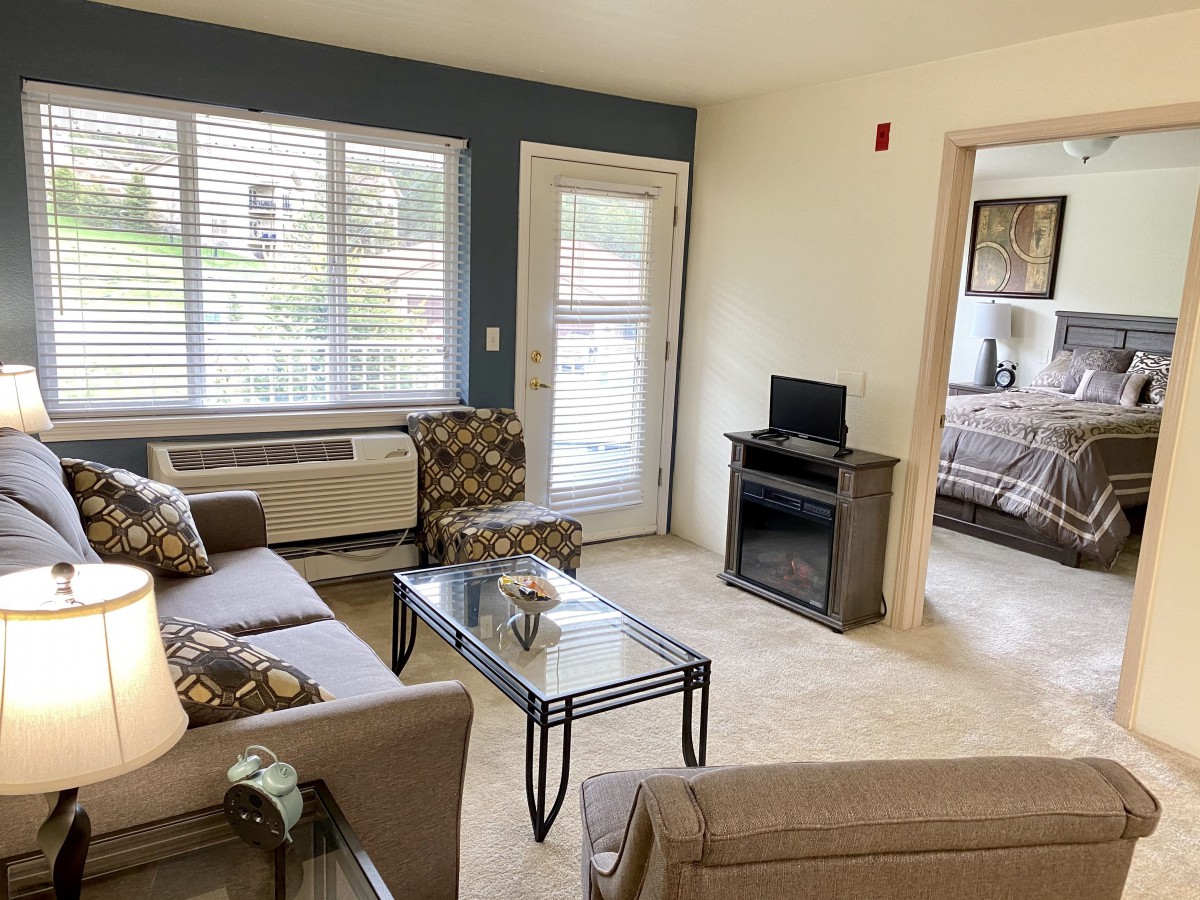 A cozy living room with a sofa, chairs, and a coffee table, offering a view into an adjacent bedroom.