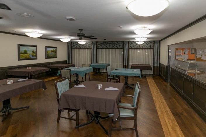 An empty dining room with neatly arranged tables and chairs, illuminated by ceiling lights.