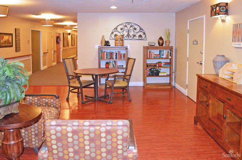 A cozy interior space featuring a wooden floor, shelves with books and decor, a round table with chairs, and comfortable seating.