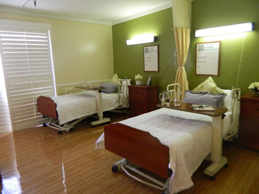 A view of a hospital patient room featuring two adjustable beds and a calming green color scheme.