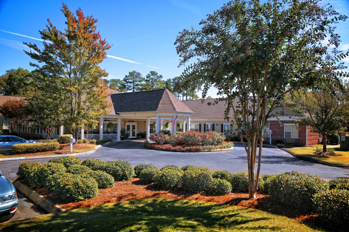 A well-maintained building entrance surrounded by lush greenery and a circular driveway.
