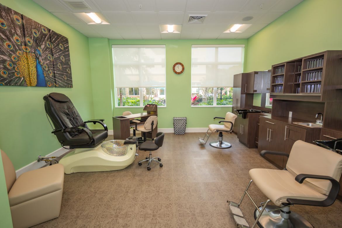 A peaceful nail salon featuring a massage chair and manicure stations with a soothing green color scheme.