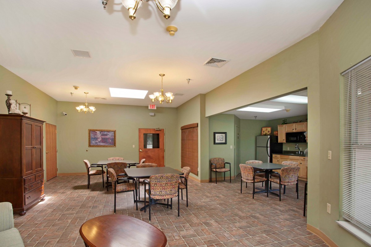 A spacious dining area with a kitchen, featuring tables and chairs under chandeliers.