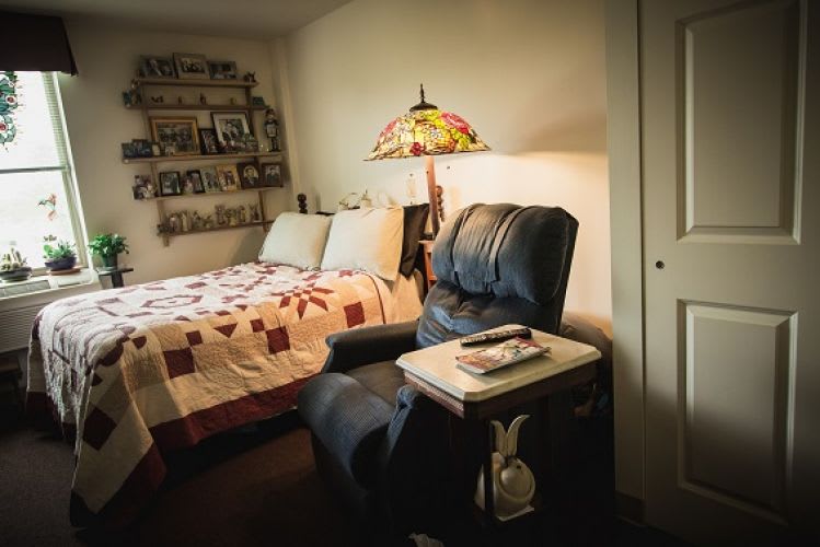A cozy bedroom with a quilt-covered bed, recliner, and a decorative lamp.