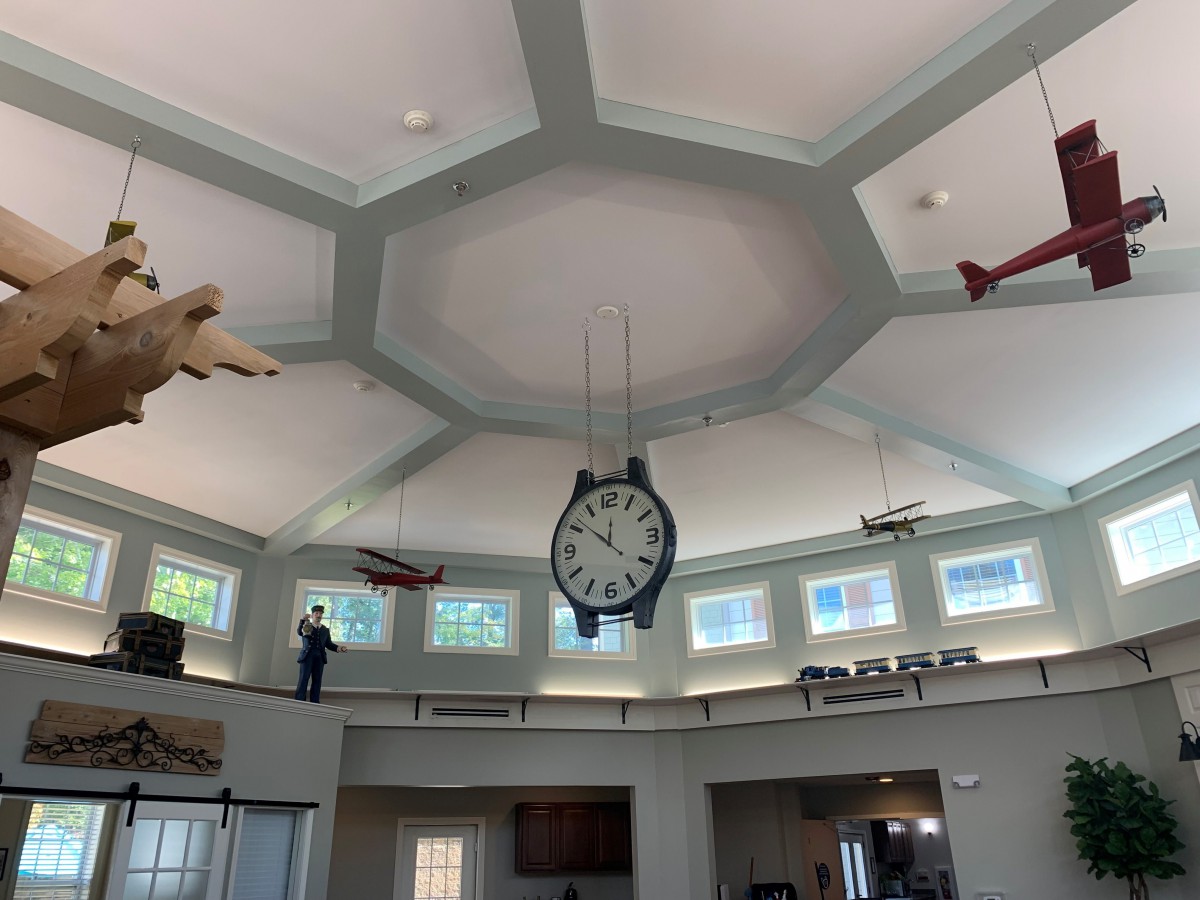 A large clock is suspended from the ceiling in a room decorated with model airplanes.