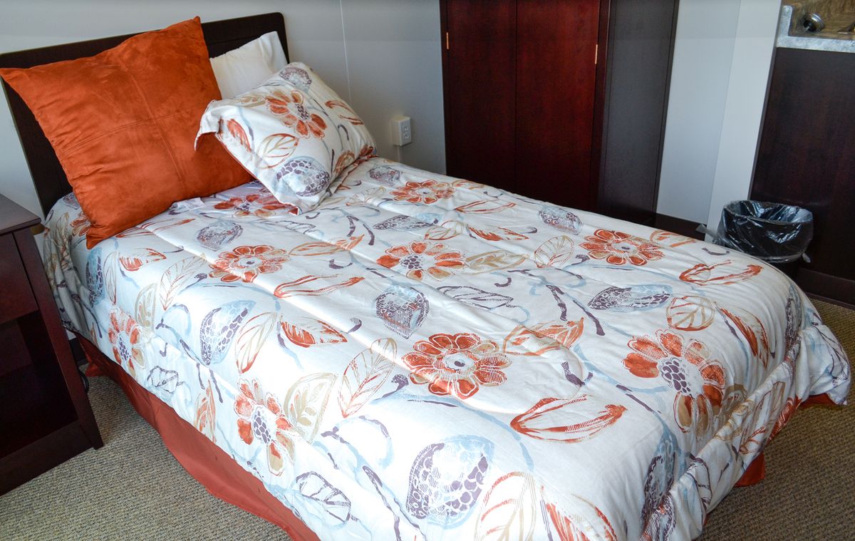 A neatly made bed with floral patterned sheets and an orange pillow in a bedroom.