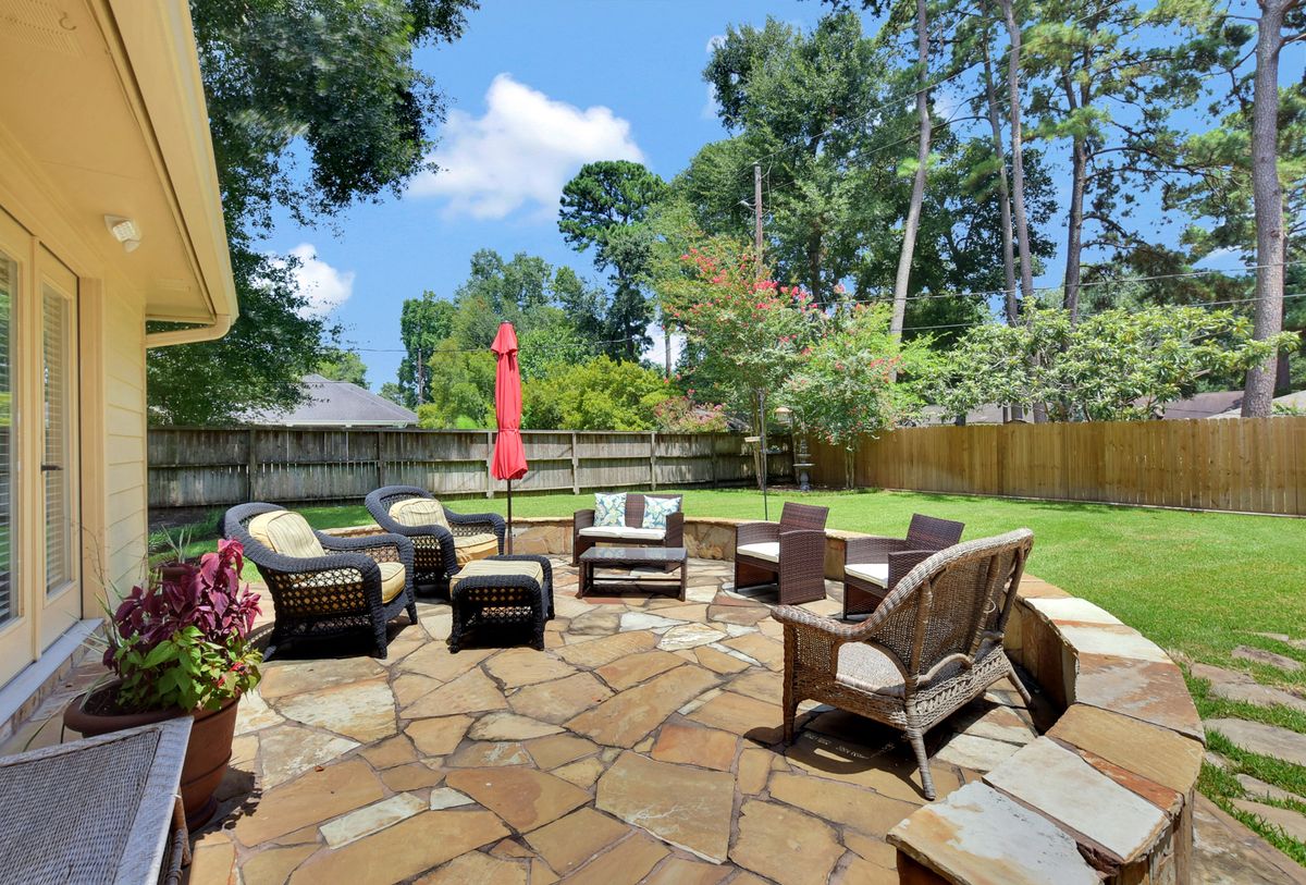 A cozy backyard patio with outdoor furniture, surrounded by a lush garden and trees.