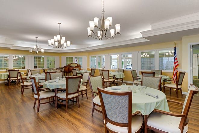 A spacious and elegantly designed dining area with neatly arranged tables and chairs, illuminated by stylish chandeliers.