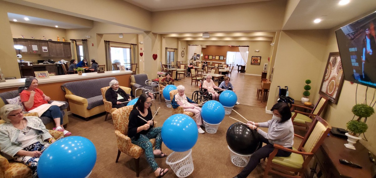 A group of seniors participating in a wellness drumming exercise using fitness balls.