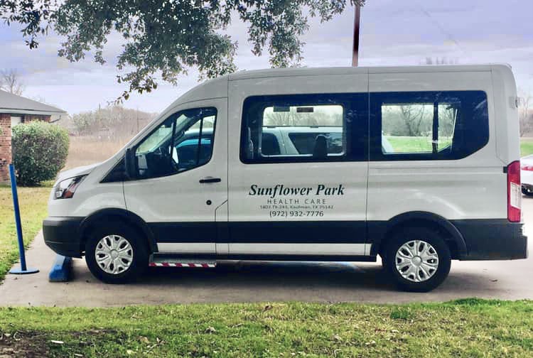 A white van parked on a grassy area under a tree, with 'Sunflower Park' written on the side.