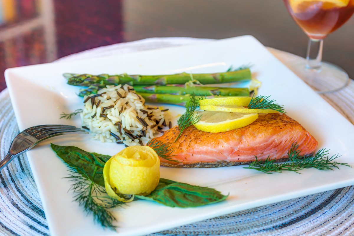 A gourmet meal featuring grilled salmon with lemon slices, asparagus spears, and wild rice, garnished with fresh dill.