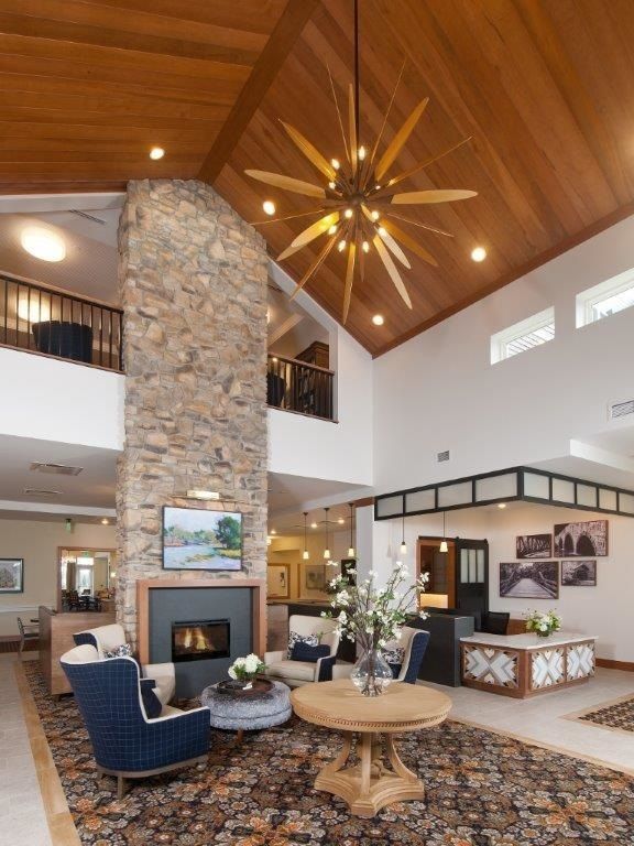 A modern living room featuring a large stone fireplace, high ceilings with a wooden finish, and a stylish chandelier.