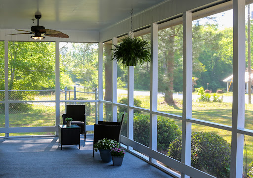 A serene screened-in porch with comfortable seating and hanging plants, inviting relaxation in a sunlit environment.