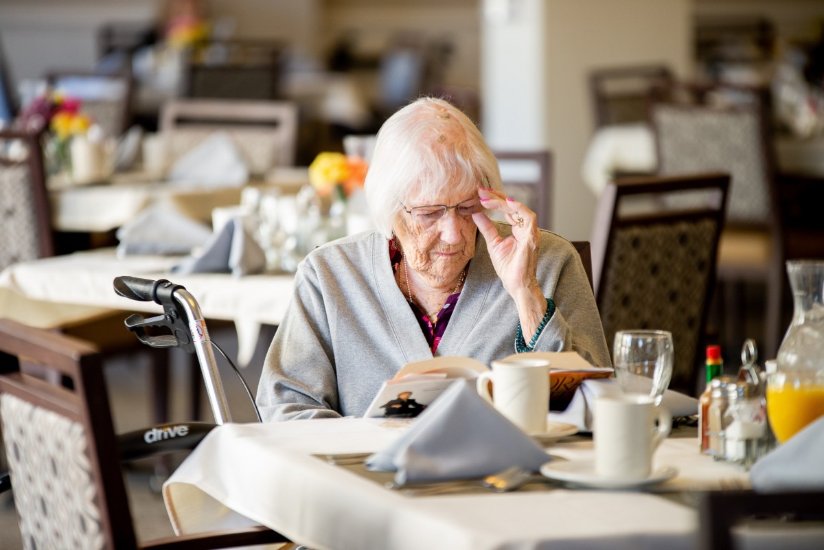 An elderly woman reading at a dining table in a restaurant setting.