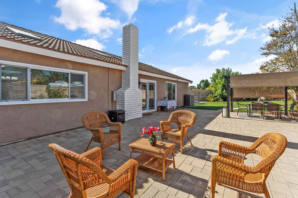 A cozy outdoor patio area with wicker furniture and a chimney, set against a sunny garden backdrop.