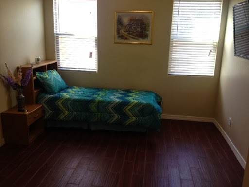 A cozy bedroom featuring a single bed with a colorful blanket and ample natural light from the windows.