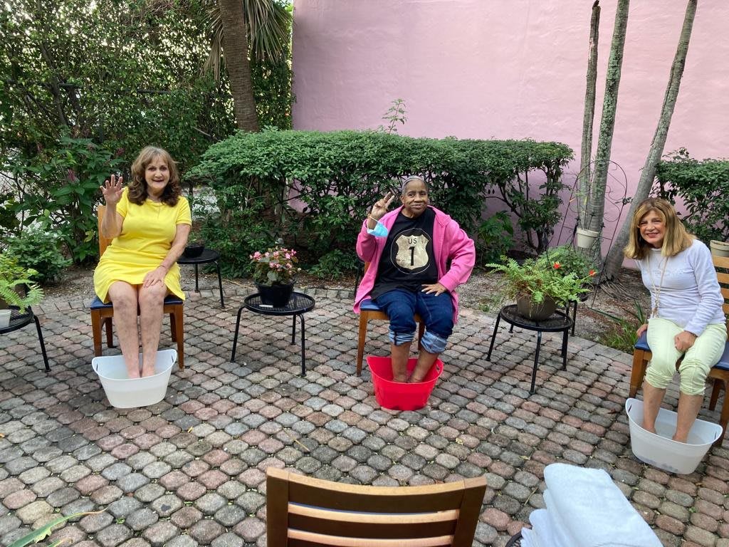 Two people enjoying a relaxing foot bath on a brick patio surrounded by plants.