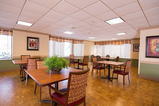 A spacious dining room featuring wooden tables and comfortable chairs, illuminated by natural light through large windows.