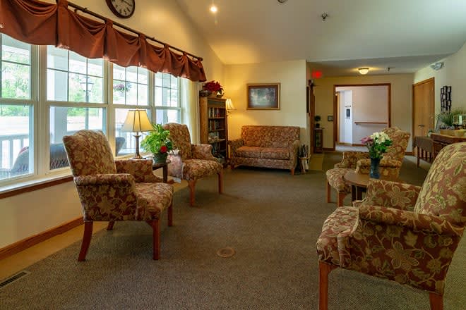 A cozy seating area with patterned chairs and sofas, illuminated by soft lighting from lamps near large windows.