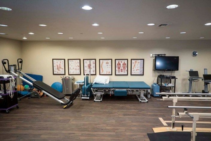 A physical therapy clinic with exercise equipment and anatomical posters.
