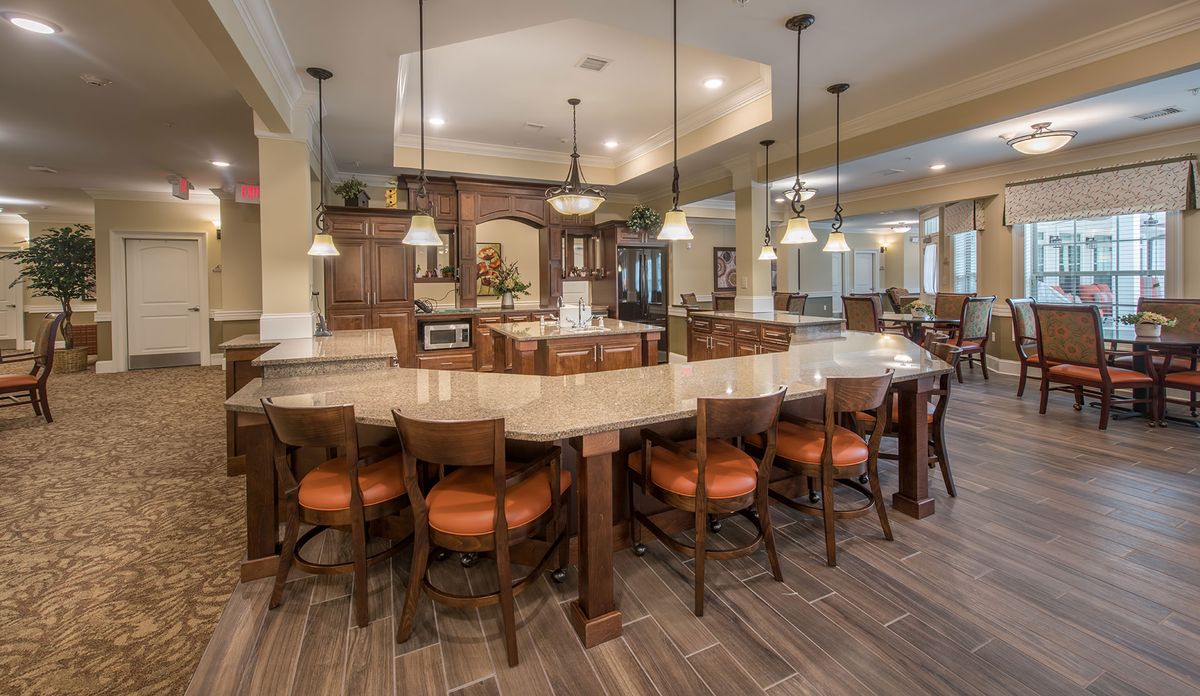 A spacious modern kitchen and dining area with a large curved countertop and multiple chairs, illuminated by pendant lights.