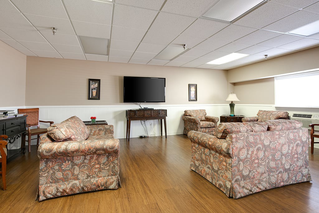 A cozy living room with patterned sofas and a flat-screen TV mounted on the wall.