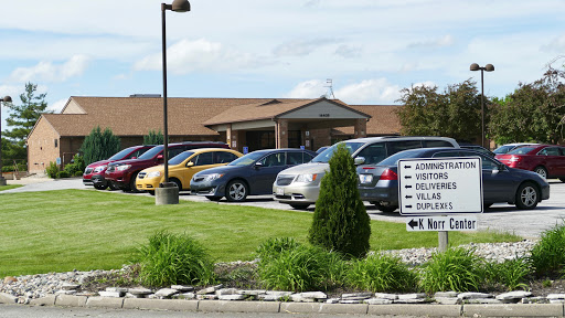 A view of parked cars in front of a building with a green lawn and signage.