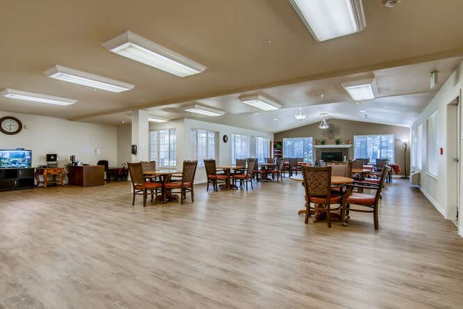 A spacious and well-lit dining area with wooden flooring and multiple tables and chairs arranged neatly.