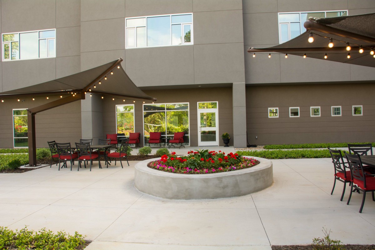 A modern outdoor patio with comfortable seating, featuring string lights and a central flower bed.