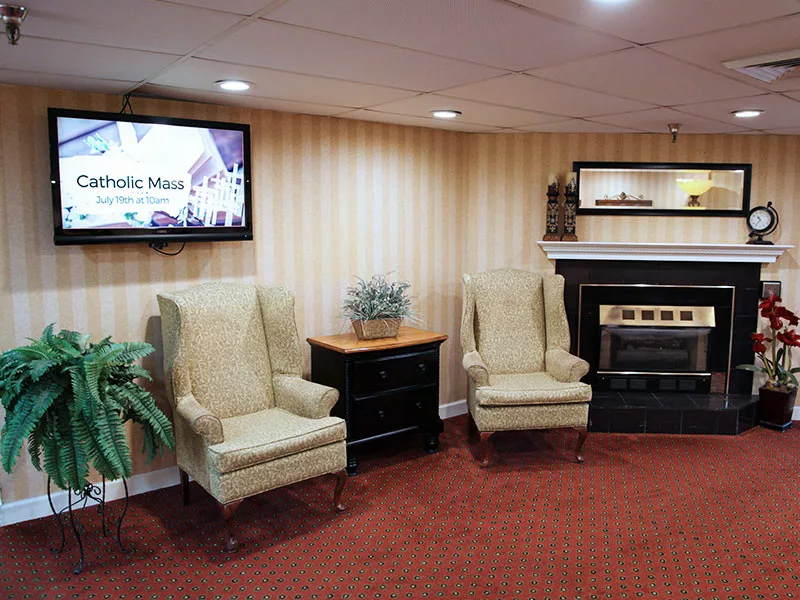A cozy seating area with two armchairs, a small table, and a fireplace, adjacent to a television mounted on the wall.