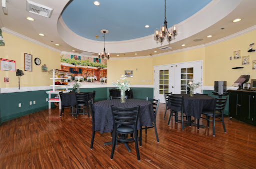 A cozy dining room setup featuring tables and chairs, illuminated by elegant chandeliers, with a bar area in the background.