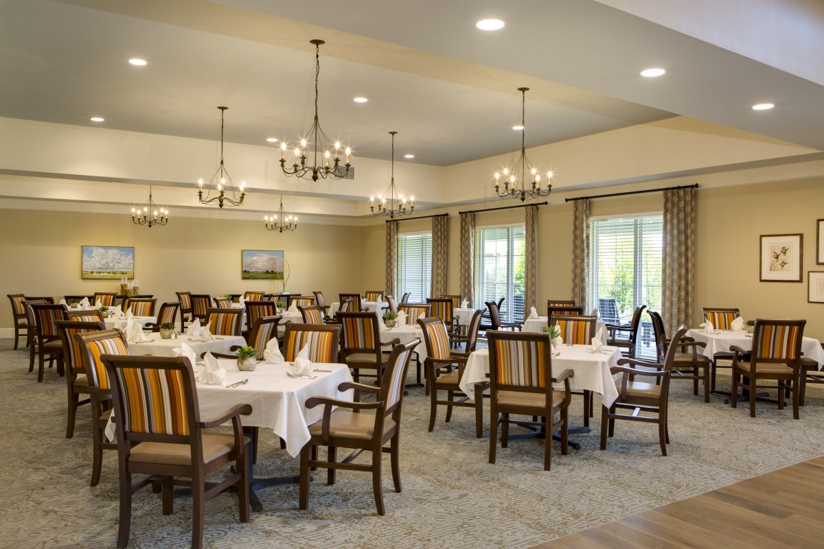 A spacious and elegantly designed dining room with neatly arranged tables and chairs, illuminated by chandeliers.