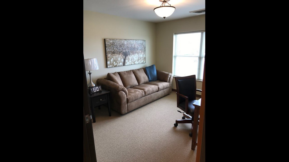 A cozy living room with a sofa, desk chair, and window providing natural light.