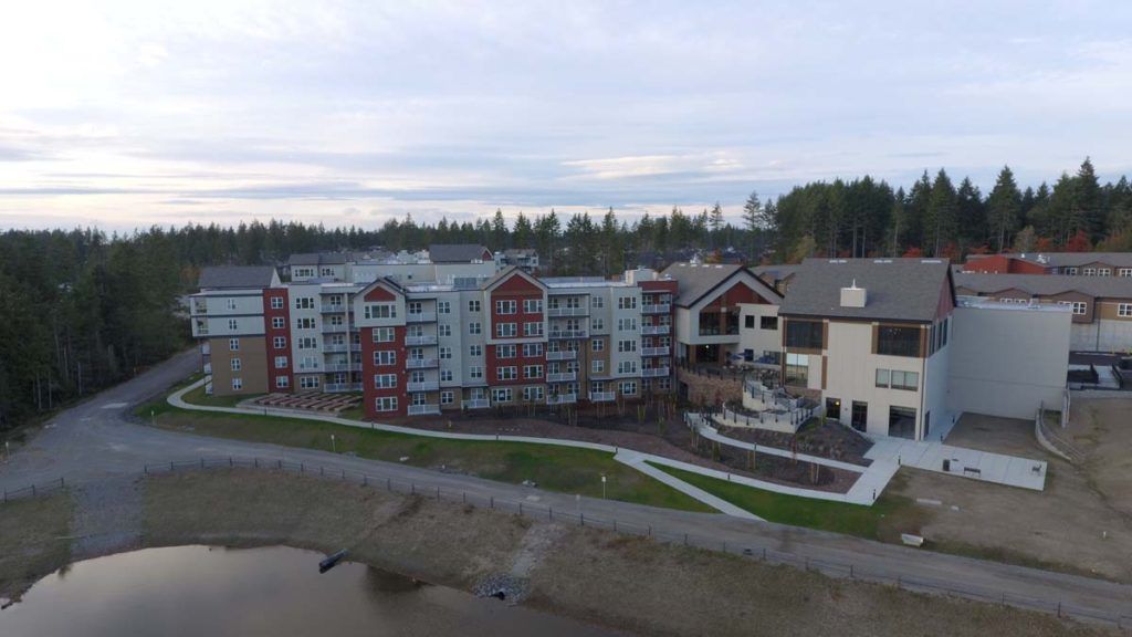 A modern apartment complex situated by the lakeside, surrounded by trees.