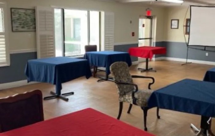 A room with several tables covered in red and blue tablecloths, surrounded by chairs.