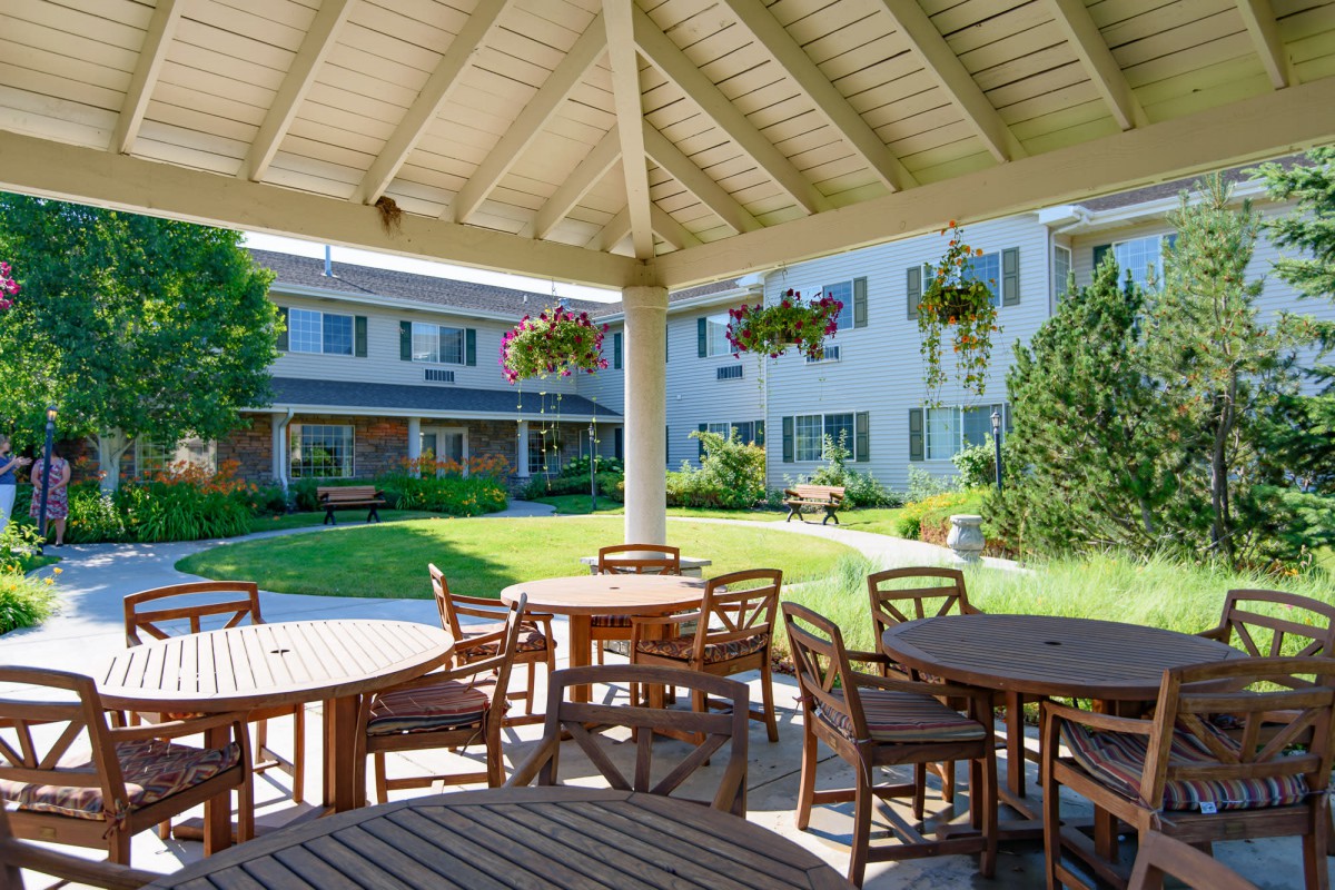 A peaceful outdoor seating area with wooden tables and hanging plants under a gazebo.