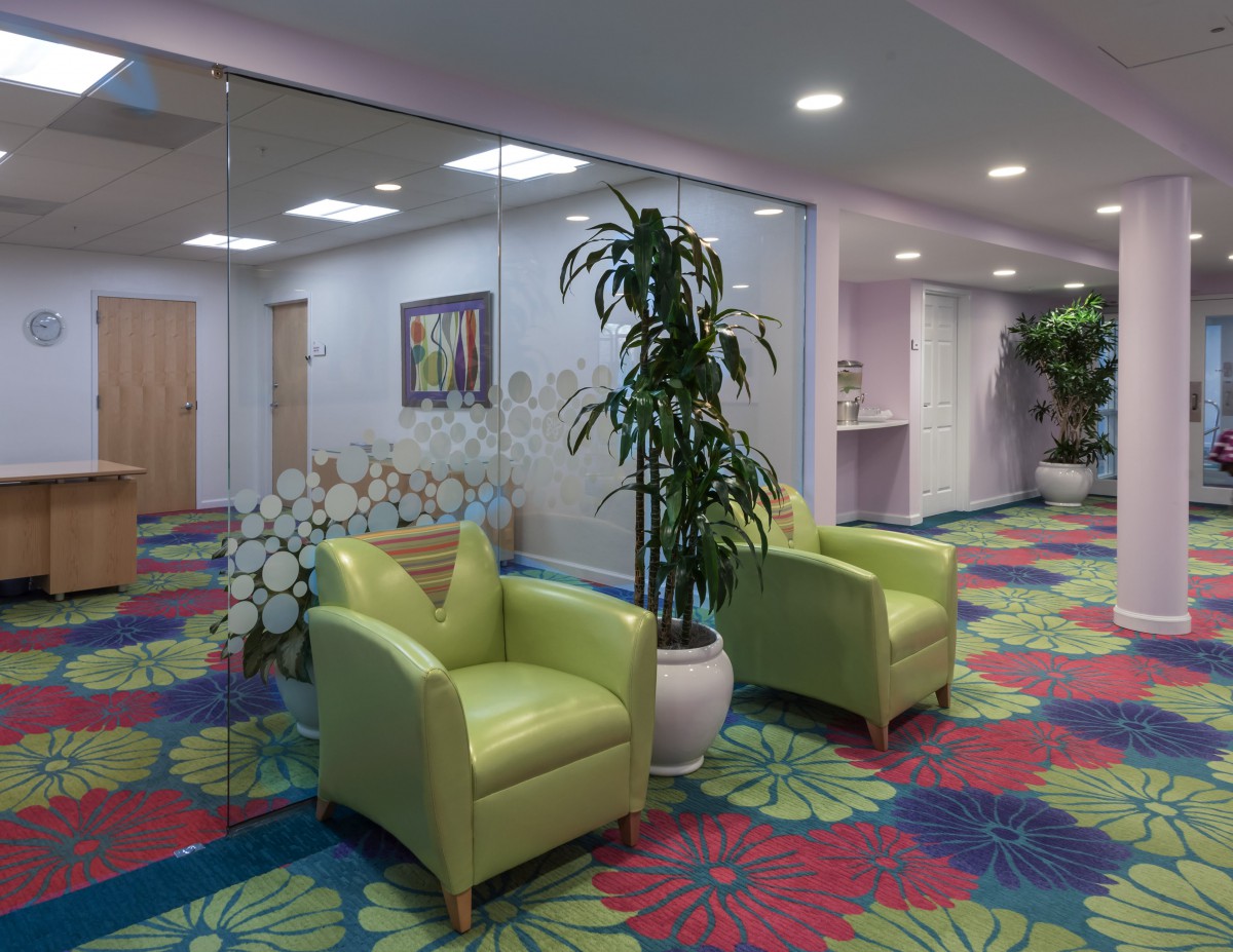 A colorful lobby with green chairs and vibrant floral-patterned carpet.