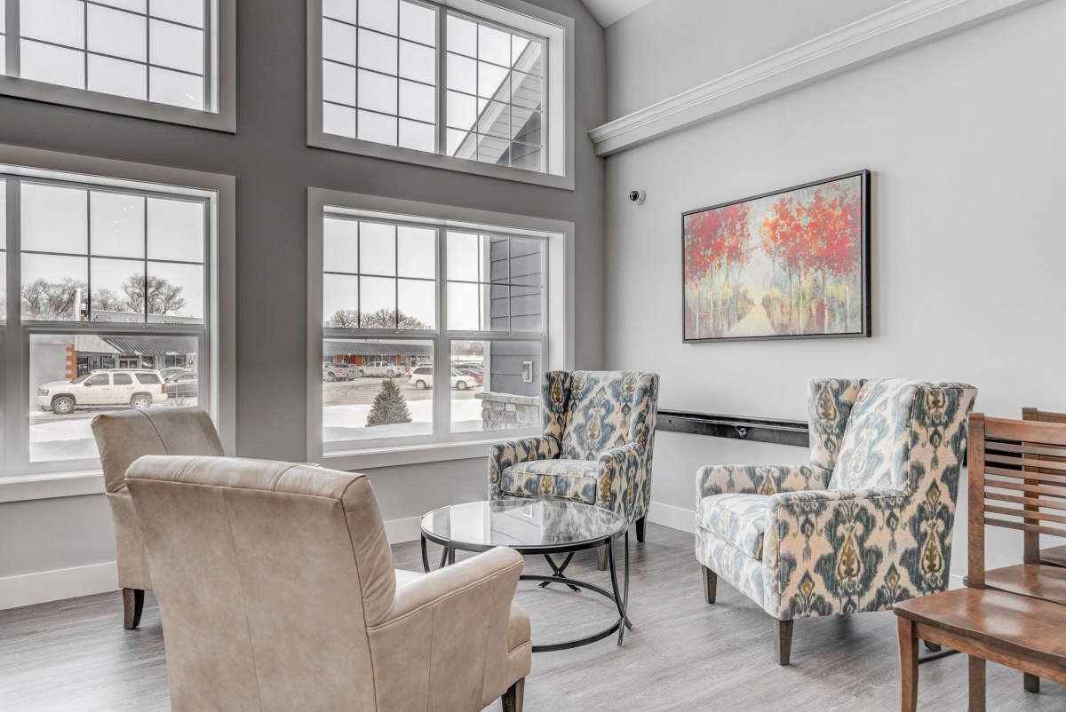 A modern living room with large windows, armchairs, and colorful artwork.
