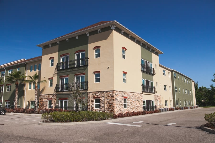 A modern apartment building with a beige and green facade under a clear blue sky.