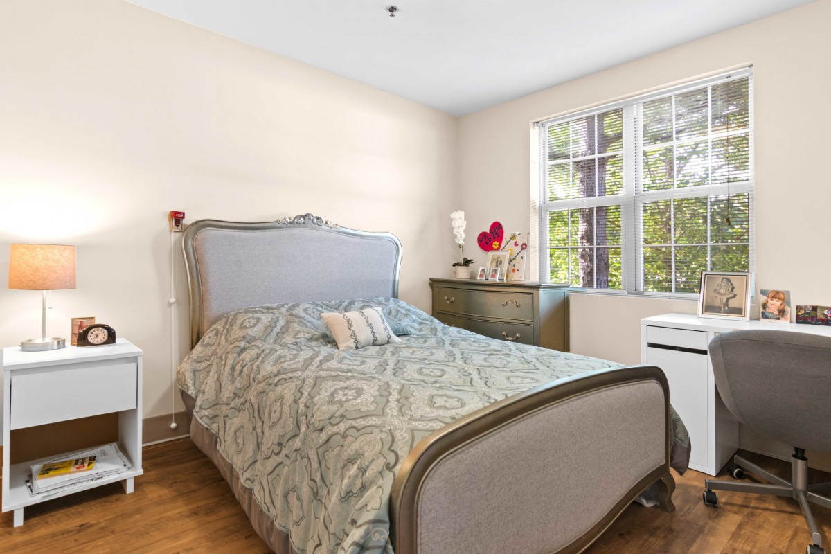 A cozy bedroom with a stylish bed, dresser, and large window allowing natural light.