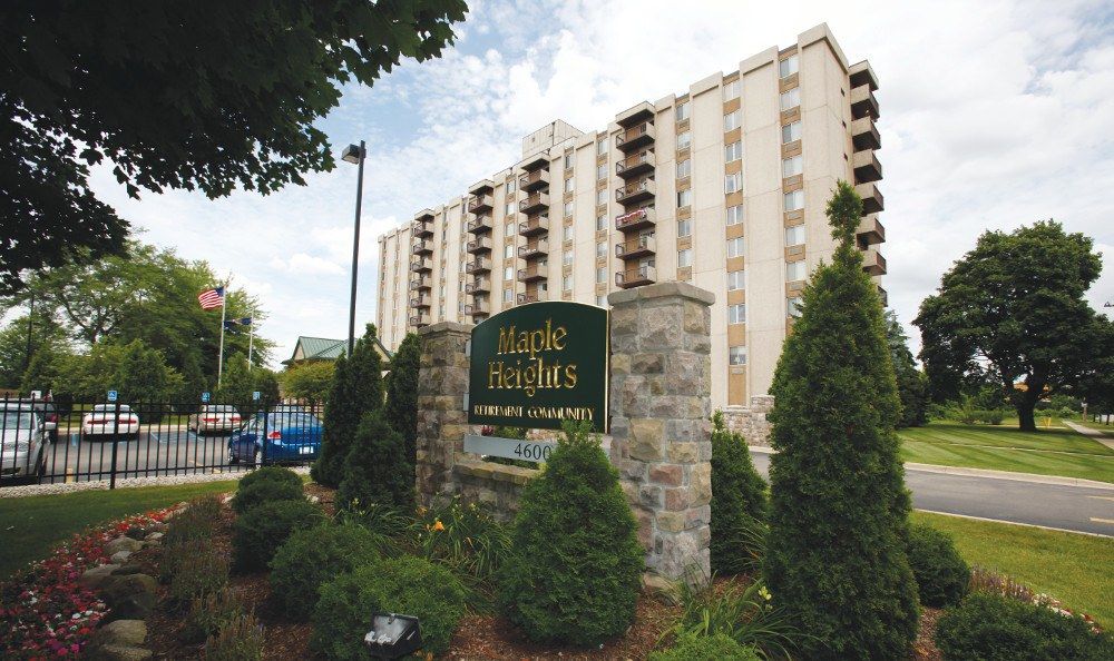 A multi-story residential apartment building with surrounding trees and a prominent sign in the foreground.