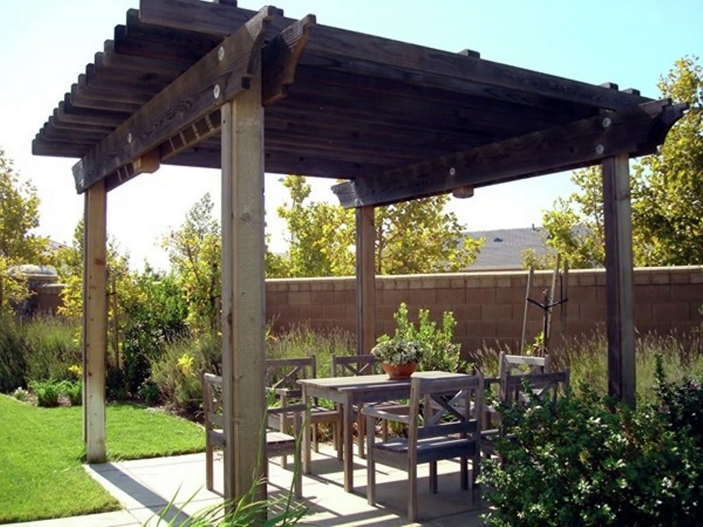 A cozy backyard patio with a wooden pergola providing shade over an outdoor seating area.