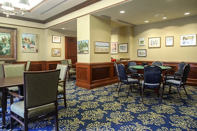 A well-lit room with several tables and chairs, adorned with artwork on the walls and featuring a patterned carpet.