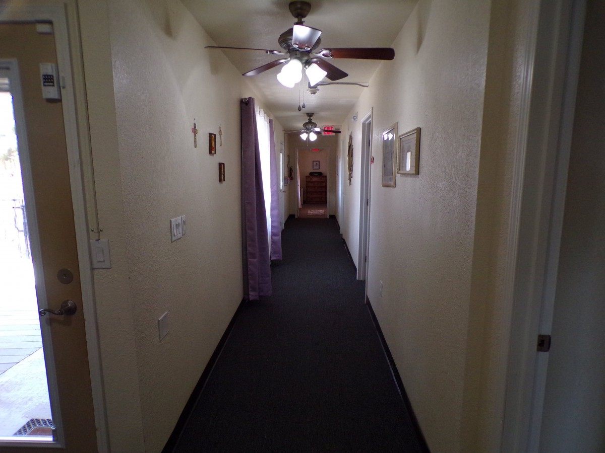 A long, carpeted hallway with ceiling fans and multiple doors.